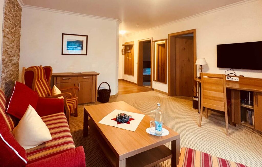 Suite im Hotel Sonne Baiersbronn mit Doppelbett, rotem Sessel, Schreibtisch, Tageslicht durch Fenster.