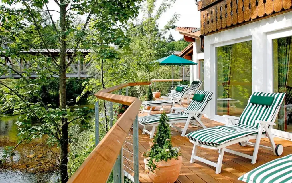 Balkon mit weißer Sitzgruppe und rundem Tisch, Blick auf umliegende Natur, rote Markise leicht eingefahren.